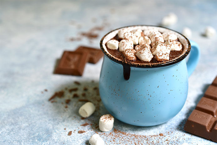 A blue mug of hot chocolate with chocolate dripping down the side and filled with marshmallows