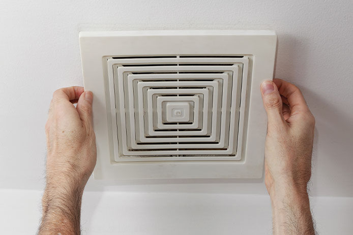 A man holding up a simple white exhaust fan in a bathorom 