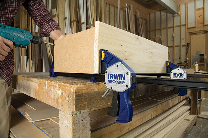 A lifestyle image of a man in a wood shop using Irwin Quick-Grip clamps to hold together two pieces of wood while making a dresser drawer