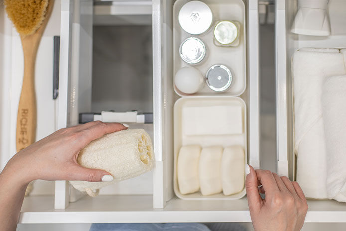 Top view of woman hands neatly organizing bathroom amenities and toiletries in drawer or cupboard in bathroom. Concept of tidying up a bathroom storage by using Marie Kondo's method.