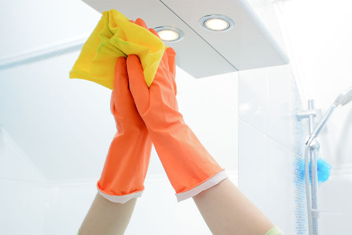 A woman polishing glass using a cleaning sponge and rubber gloves cleaning a mirror with a spray cleaner