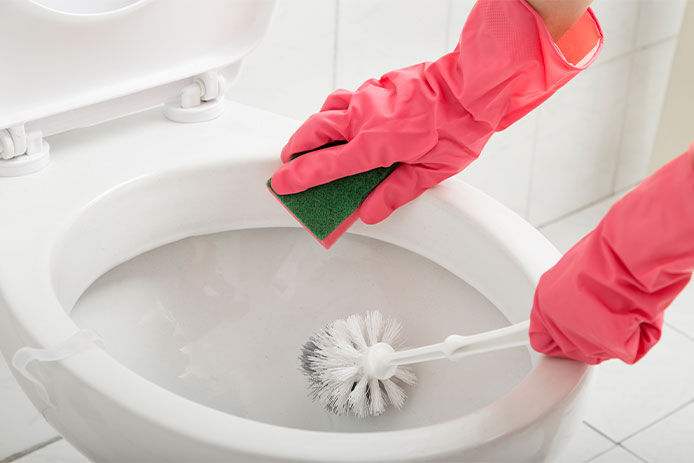 Close up of female hands wearing protective gloves, scrubbing toilet with sponge and brush