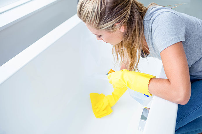 Woman wearing yellow rubber gloves cleaning her tub