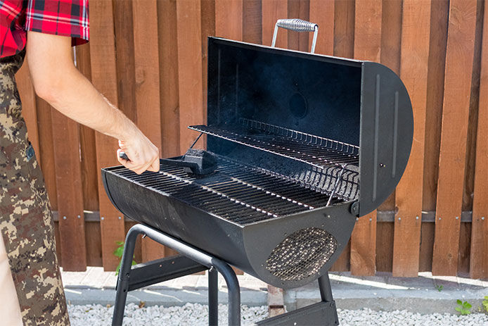 A close up of a man cleaning a charcoal grill with a wire brush