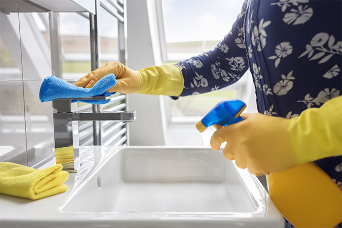 Person wearing latex cleaning gloves while spraying and wiping down a bathroom sink