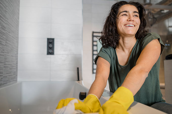 Woman smiling, wearing yellow rubber cleaning gloves while cleaning bathtub