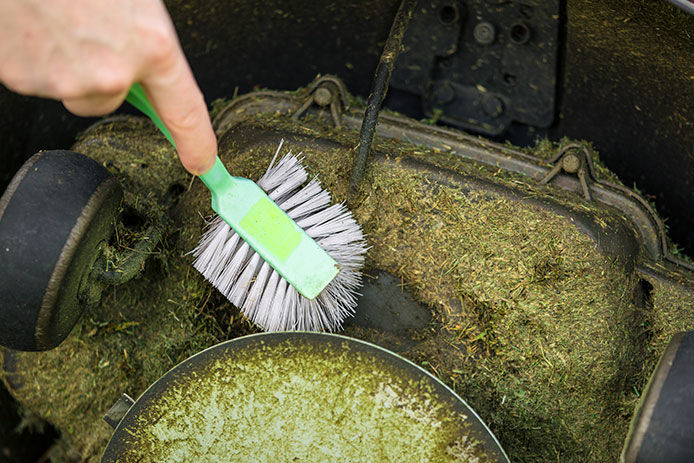 Cleaning grass off of the bottom of mower deck with a brush