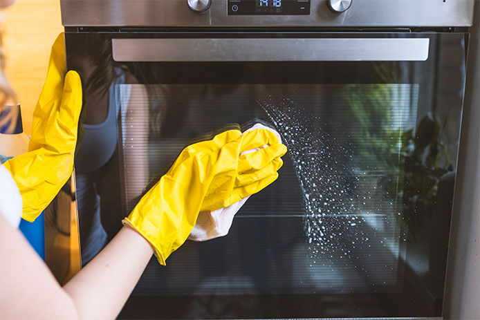 Person wearing yellow rubber cleaning gloves wiping down the glass on the outside of the oven