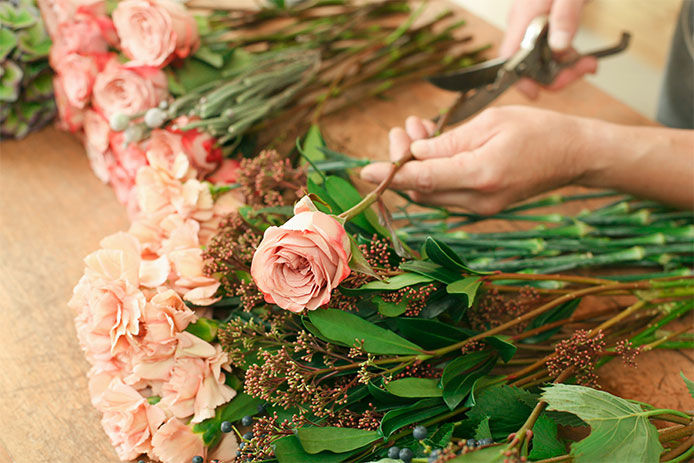 Flowers delivery, creating order. Male florist hands closeup, cuts rose for bouquet in flower shop.