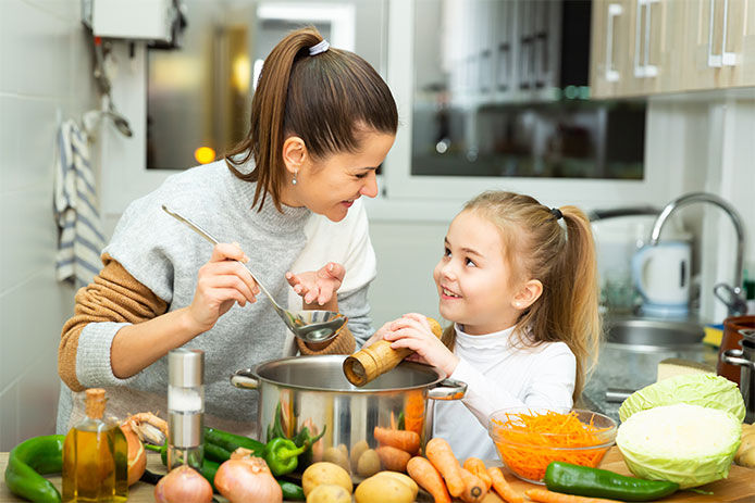 Positive mother and little daughter tasting soup together