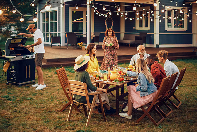 Parents, Children, Relatives and Friends Having an Open Air Barbecue Dinner in Their Backyard. Old and Young People Talk, Chat, Have Fun, Eat and Drink. Garden Party Celebration in a Backyard.