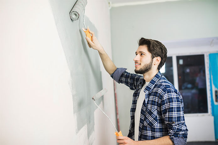 Young handsome man painting wall with paint roller