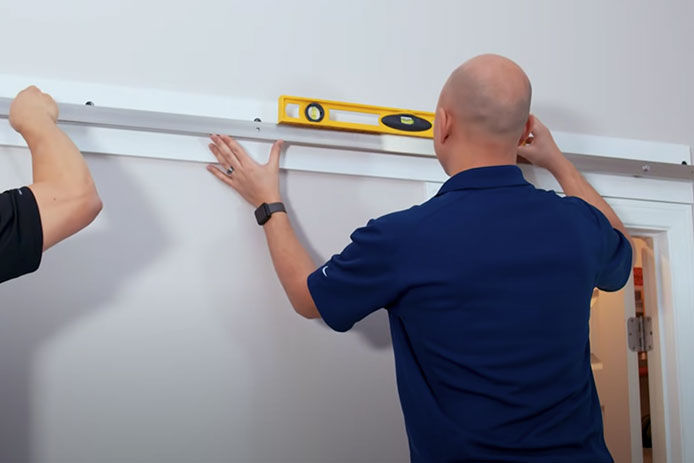 Two people measuring and using a level to install the track of a barn door kit 