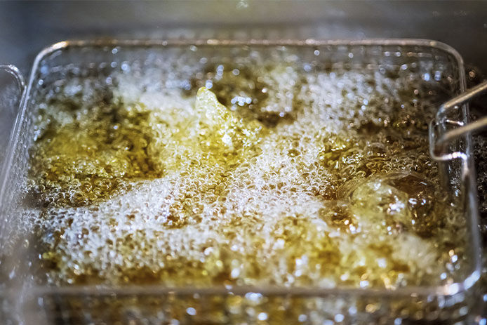 A basket of tan-colored food is frying in hot, bubbling yellow oil.