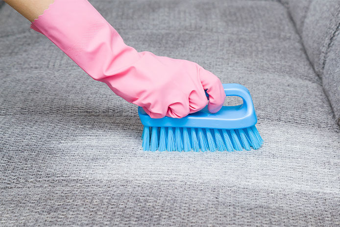 A person scrubbing a couch with a brush