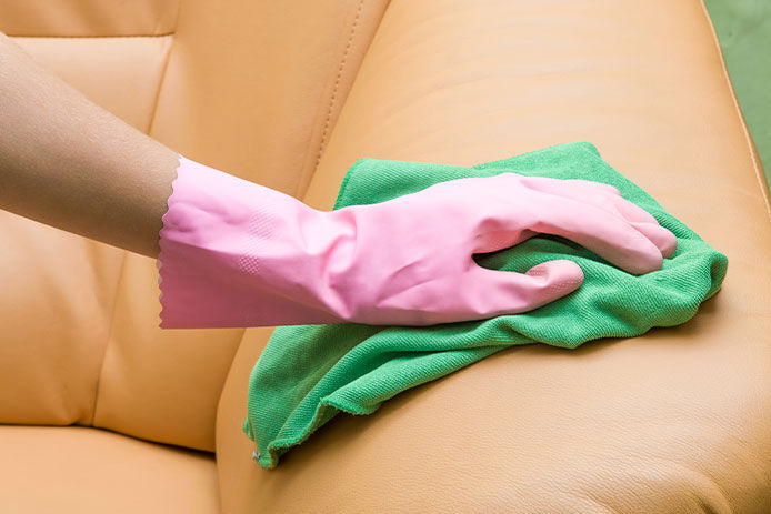 A person wiping a couch with a green cloth