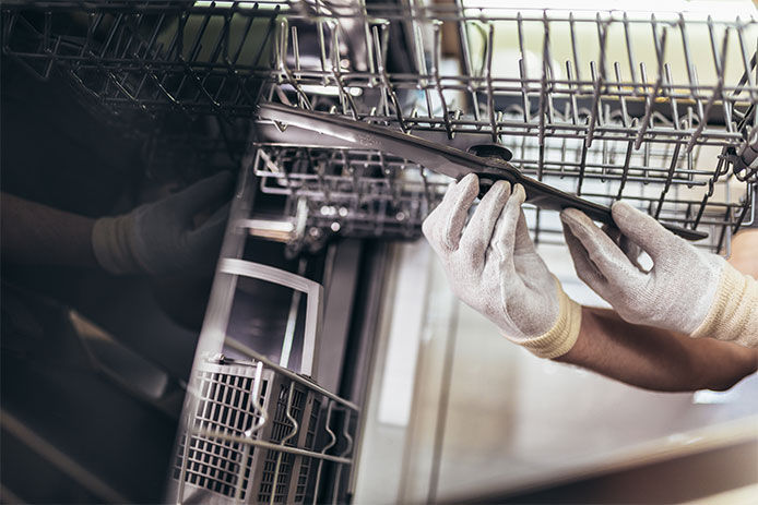 Male Technician Repairing Dishwasher In Kitchen, close up.