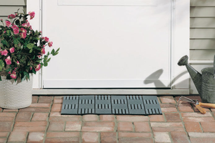 A close up view of the bottom of a white front door with a welcome mat, flower pot, and watering can