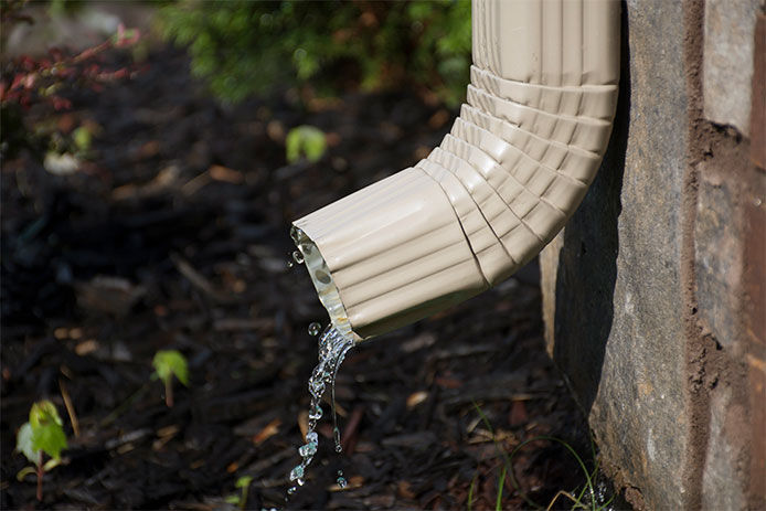 A close up image of a white downspout on a home dripping water 