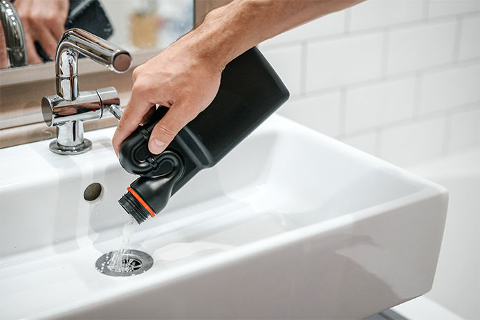A person pouring liquid drain cleaner down a sink drain
