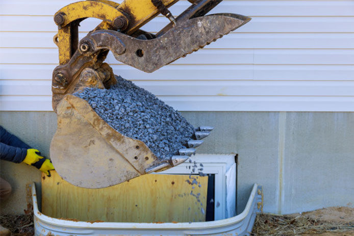 An excavator adding crushed rocks to the surrounding of an egress window