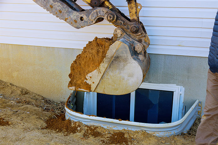 An excavator digging out a hole on the side of a home to install and Egress window