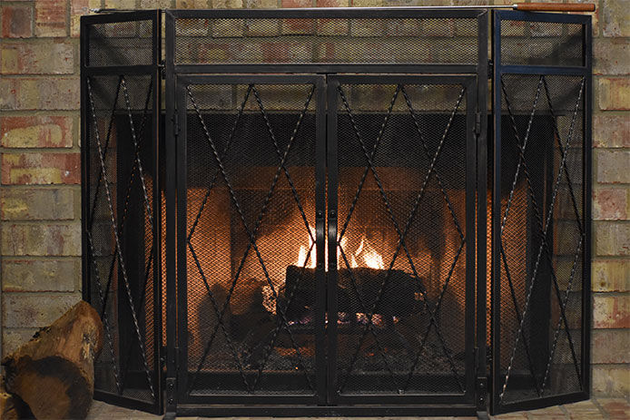 A brick fireplace with a black fireplace screen in front of it