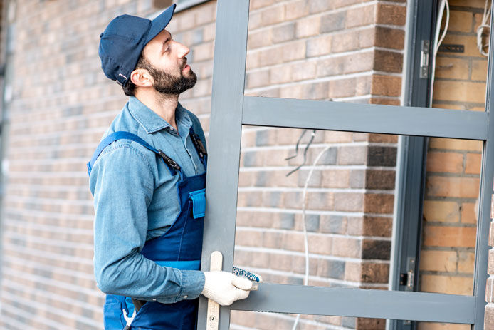 Builder in uniform installing aluminium entrance door of a new house outdoors