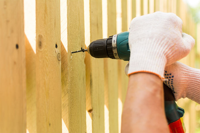 A man using a power drill to screw a screw into a fence panel