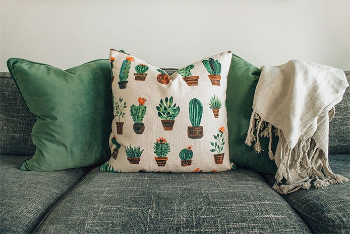 Shallow focus of cactus print fabric cushion seen on a modern sofa, seen in a bright, sunny living room.