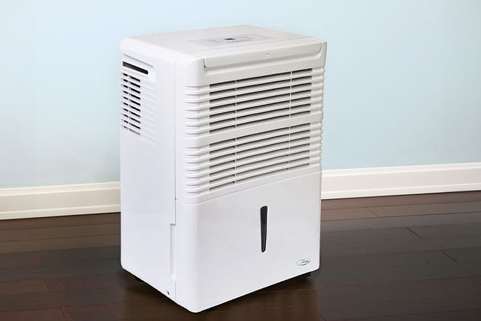 A white dehumidifier sitting on top of dark wooden floors and bright blue colored walls 