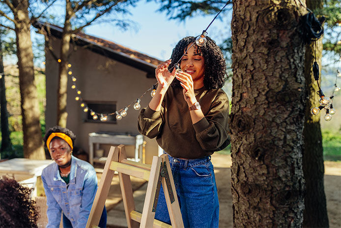 Two friends outside hanging up patio lights