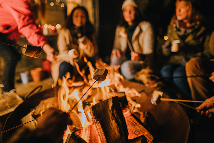 A group of friends all sitting around the firepit keeping warm and roasting marshmallows