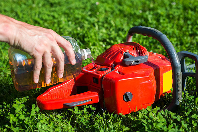 Chainsaw laying in the grass while pouring an oil/gas blend into the chainsaw