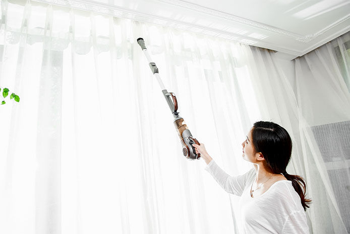 Woman dusting the top of her curtains in her living room