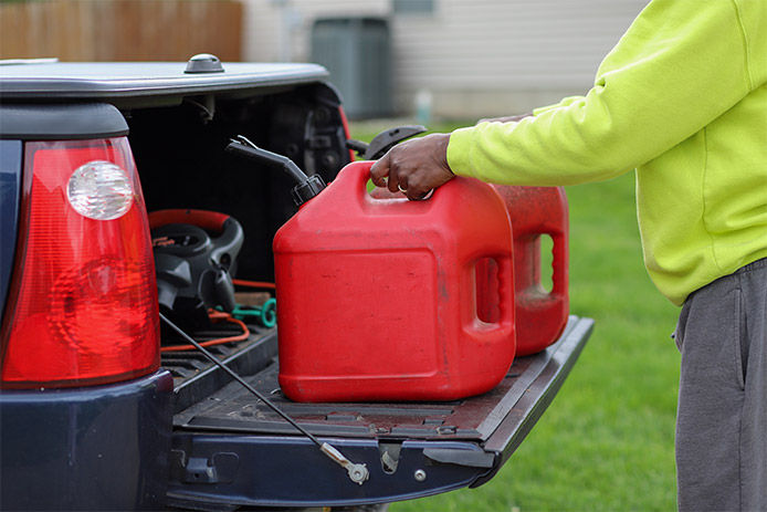 A man wearing a high vis sweater loading two gas cans into a back bed of a pickup truck