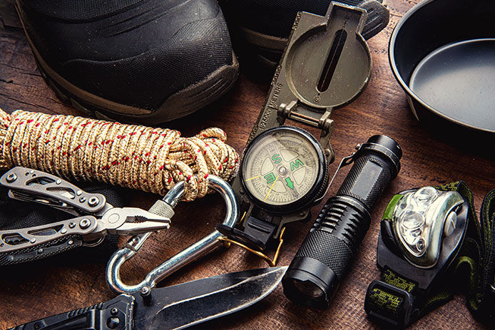 Camping tools like: compass, rope, flashlight, and folding knife on a wooden tabletop, overhead view