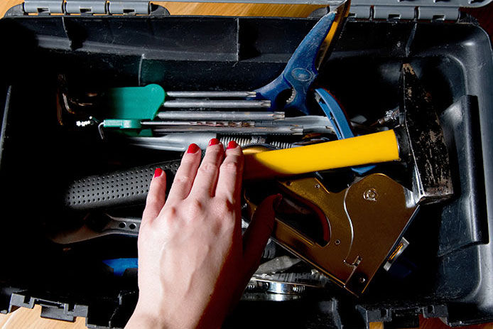 Female hand with red manicure reaches for tools in an open tool box