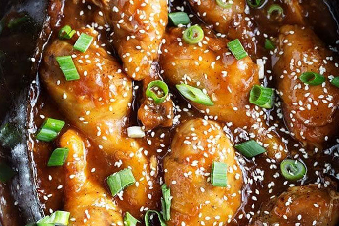 A close up image of honey garlic chicken. It is garnished with chopped green onions and seasme seeds