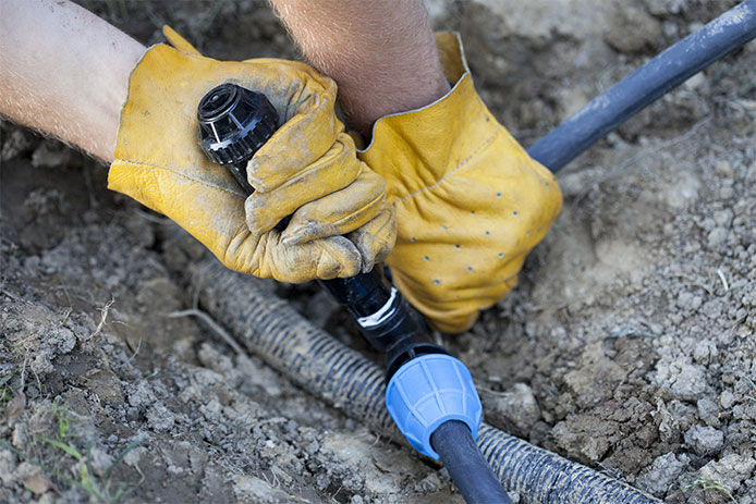 A close up image of a man wearing yellow leather hide gloves manually turning off an underground sprinkler system 