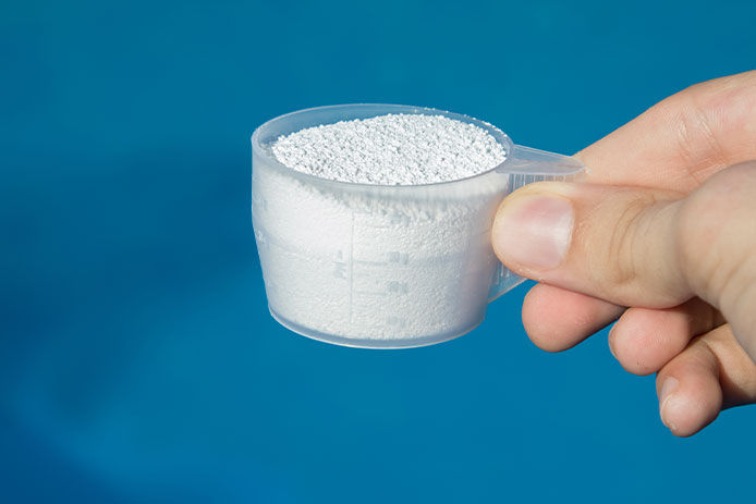 Person holding a measuring scoop of granular chlorine, close-up