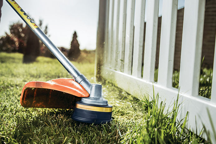 Weed wacking with a string trimmer next to a white picket fence