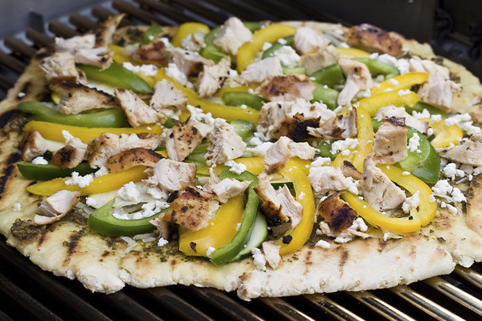 A green and yellow vegetable pizza is dotted with cheese and sits atop the silver grates of a grill.