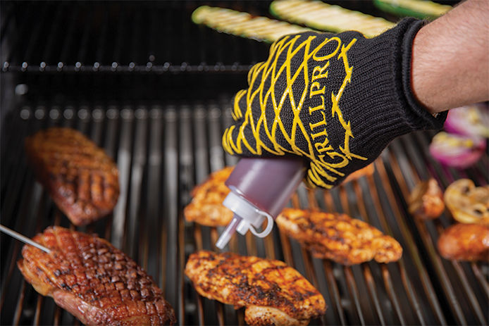 Man wearing Grill Pro grilling safety gloves and applying BBQ sauce to chicken breast on a gas grill 