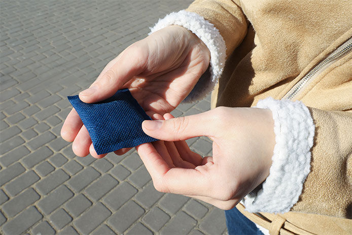 Person wearing a winter coat holding out a hand warmer in their hand