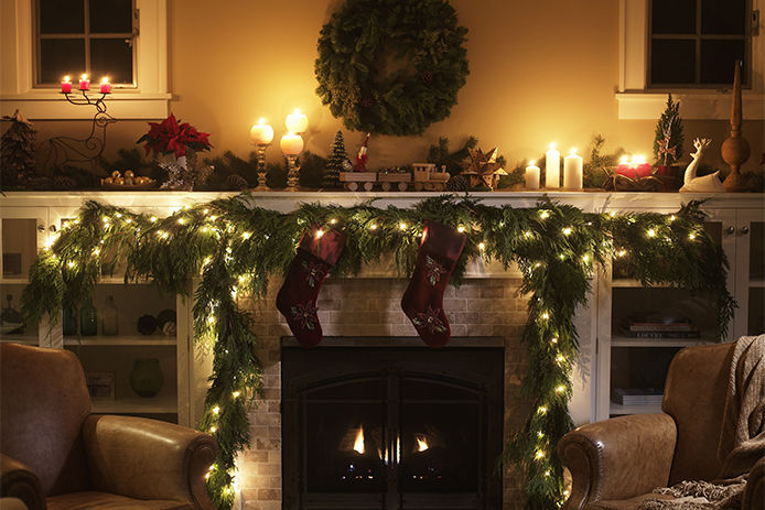 A dimmly lit living room with christmas lights, and candles lit around the fireplace and mantle