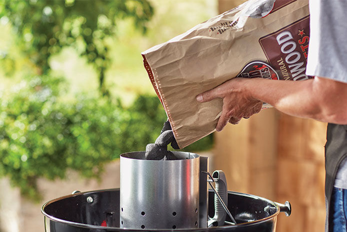 A man filing a charcoal chimney with charcoal pellets on a charcoal grill 