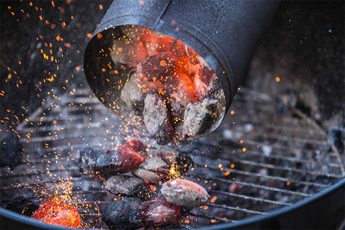 A close up image of a charcoal chimney being dumped onto a charcoal grill