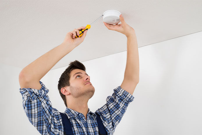 Man screwing a smoke alarm into the ceiling