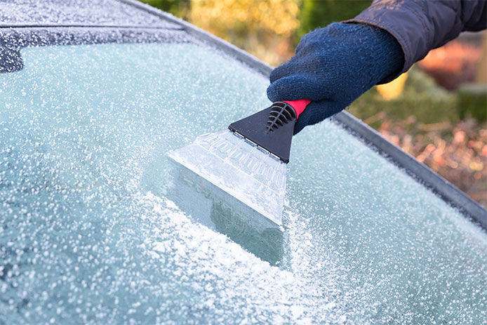 Person wearing winter gloves using a scraper on windshield for ice